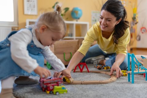 Kindergarten,Teacher,And,Toddler,Sit,On,The,Floor,Playing,With